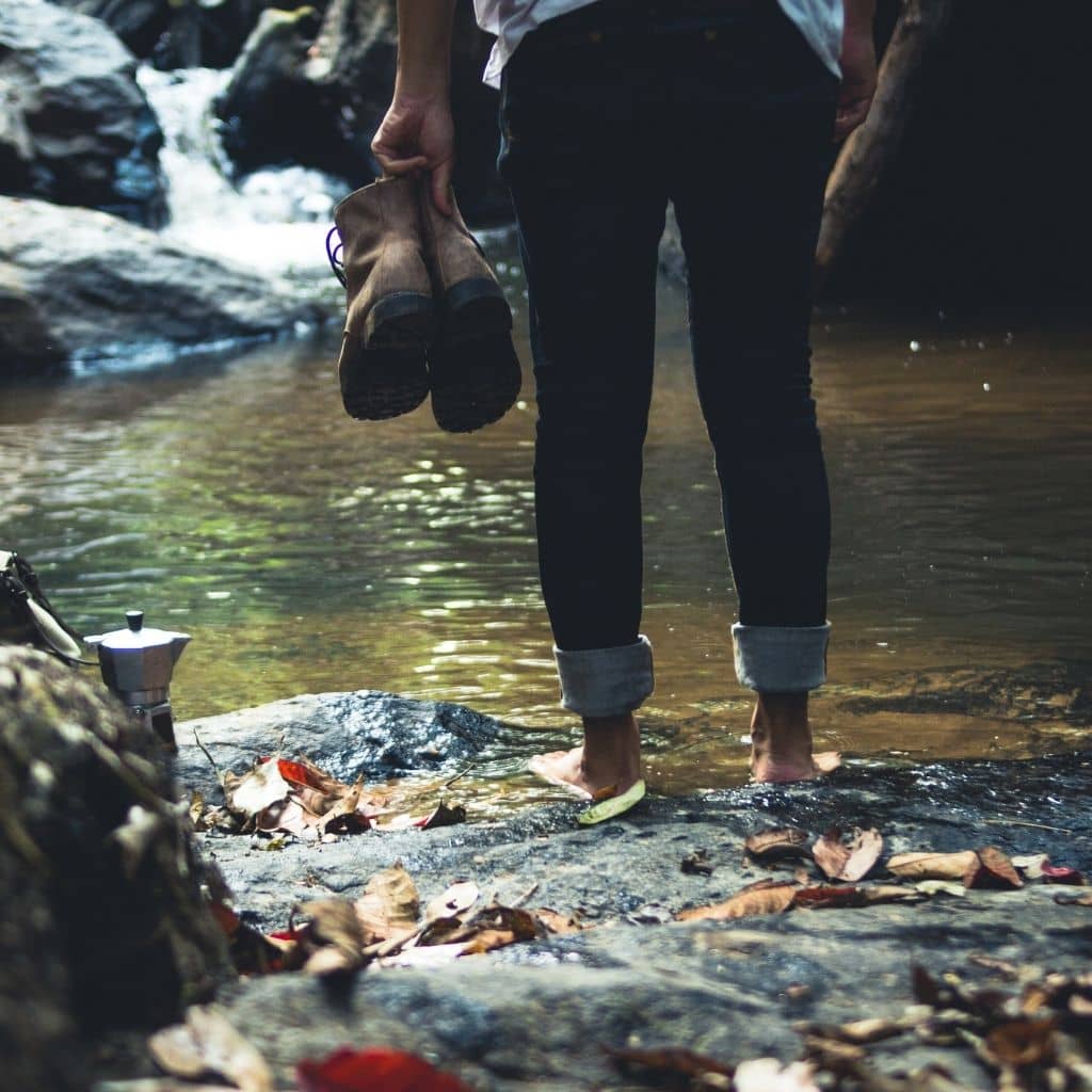 forest bathing woman walking barefoot in water wearing jeans rolled up